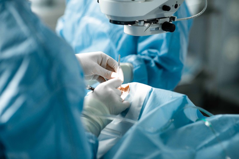 Schr&auml;ger Blick auf die H&auml;nde des Chirurgen w&auml;hrend der grauen Star Operation. Das Gesicht des Patientin ist mit einem blauen Tuch abgedeckt, der Chirurg tr&auml;gt wei&szlig;e Handschuhe und h&auml;lt ein silberfarbenes Instrument in der Hand / &copy; Till Findl